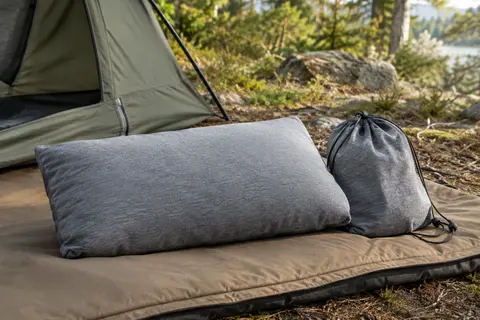 Oreiller de camping gris en coton jersey avec son sac de rangement, installé près d’une tente.