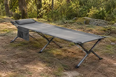 Lit de camp pliant gris avec oreiller intégré et poche latérale, installé dans une clairière