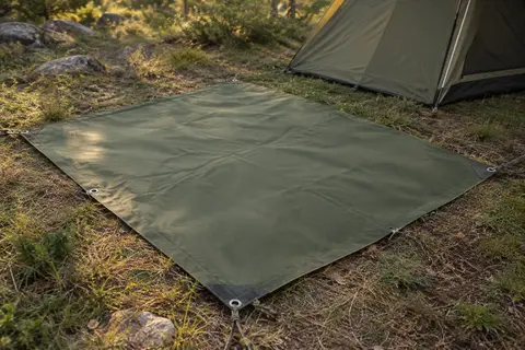 Bâche de camping verte en tissu Oxford posée dans une clairière, avec œillets et angles renforcés visibles