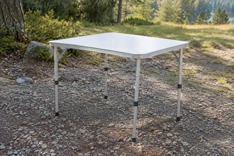 Table de camping pliante blanche avec plateau rectangulaire et pieds réglables en aluminium, installée en extérieur.