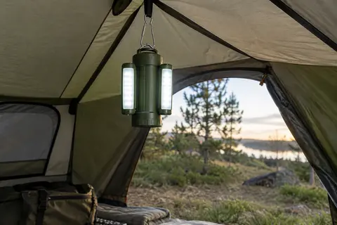 Lanterne de camping verte à panneaux latéraux dépliés, suspendue dans une tente sobre en fin de journée.