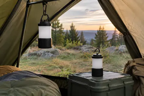 Deux lanternes de camping noires à crochet, l’une suspendue dans une tente et l’autre posée à côté.