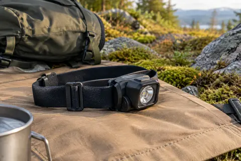 Lampe frontale noire en plastique posée sur une toile de camping sable dans une clairière