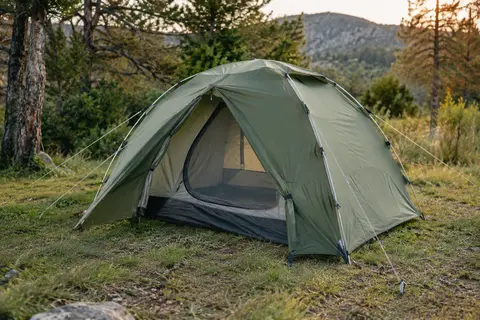Tente dôme verte pour deux personnes installée dans une clairière, avec ses vestibules et ses haubans visibles.