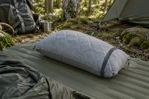 Oreiller gonflable gris à housse matelassée posé sur un matelas de camping dans un sous-bois