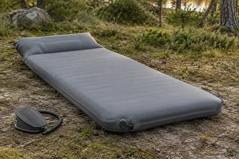 Matelas de camping gonflable gris avec oreiller intégré, installé sur le sol d’une clairière