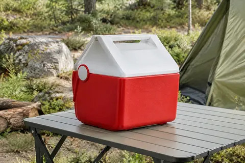 Glacière Igloo Playmate Mini rouge posée sur une table de camping dans une clairière en lumière douce.