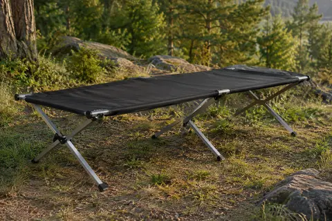 Lit de camp pliant à toile noire et structure en aluminium installé dans une clairière