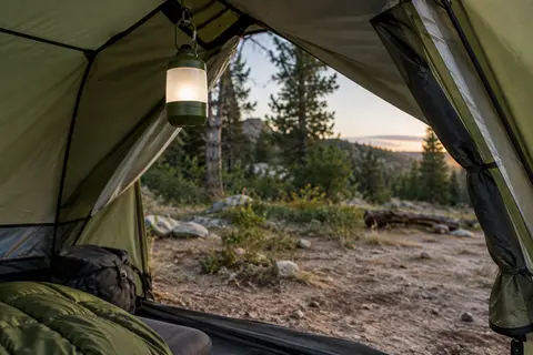 Lanterne de camping verte suspendue dans une tente ouverte, au bord d’une clairière
