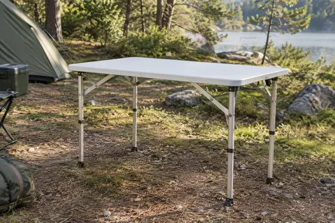 Table pliante blanche de camping avec plateau rectangulaire et structure en aluminium, installée dans une clairière