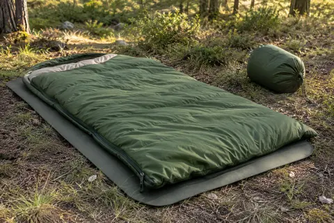 Sac de couchage Naturehike vert déplié dans une clairière, avec sa housse de rangement posée à côté