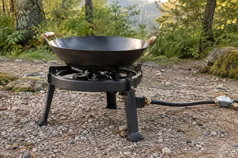 Réchaud Neruma noir en fonte à trois anneaux, posé sur un terrain de camping avec un wok