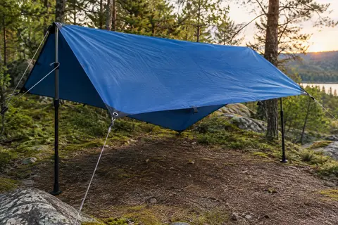 Bâche de camping bleue tendue entre des supports dans une clairière, avec ses œillets visibles.
