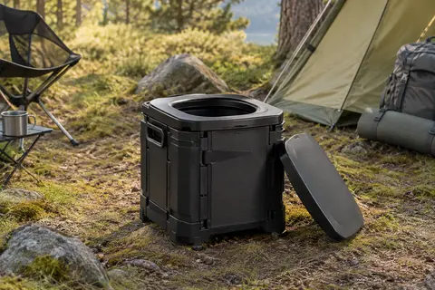 Toilette de camping portable noire et pliable, avec couvercle, installée dans une clairière