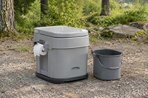 Toilette portable grise en polypropylène avec seau amovible et porte-papier, posée dans une clairière