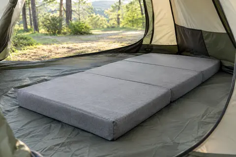 Matelas pliant gris à trois parties, déployé dans une tente de camping sur un sol sobre.