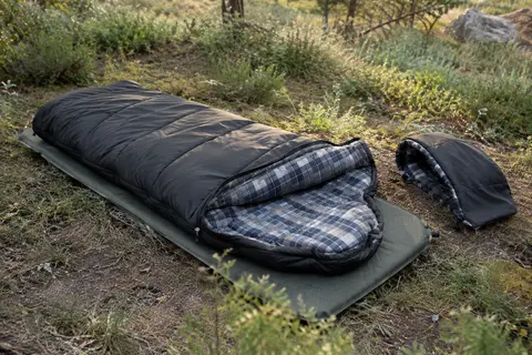 Sac de couchage rectangulaire noir en flanelle installé sur un tapis dans une clairière