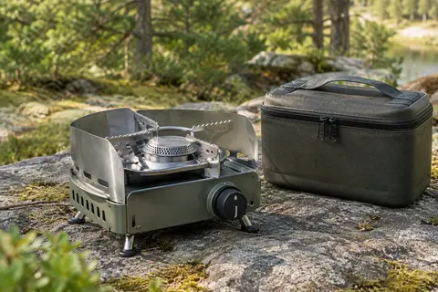 Réchaud de camping en métal avec protection contre le vent et mallette posé sur une surface minérale