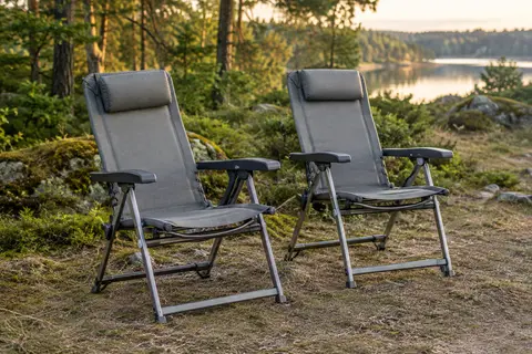 Deux fauteuils pliants gris en textilène, avec dossier inclinable et appuie-tête amovible, installés dans une clairière