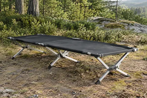Lit de camp pliant noir avec toile tendue et armature en aluminium installé dans une clairière